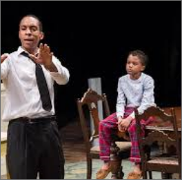 Black and white image of an adult actor playing Walter Younger and a young boy playing Travis Younger acting out a scene from 'A Raisin in the Sun' on stage 